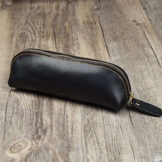 Black leather pencil case with gold zipper on a wooden surface