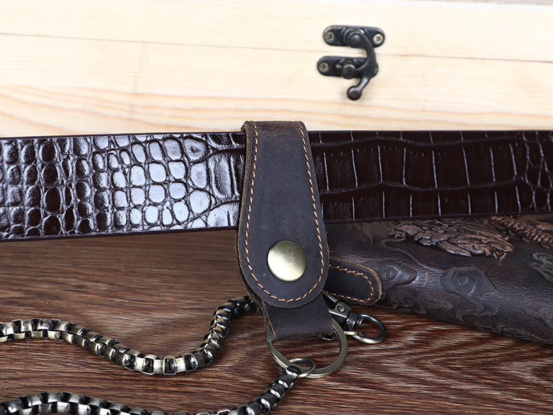 Close-up of a leather bag with crocodile texture and chain detail on a wooden surface.