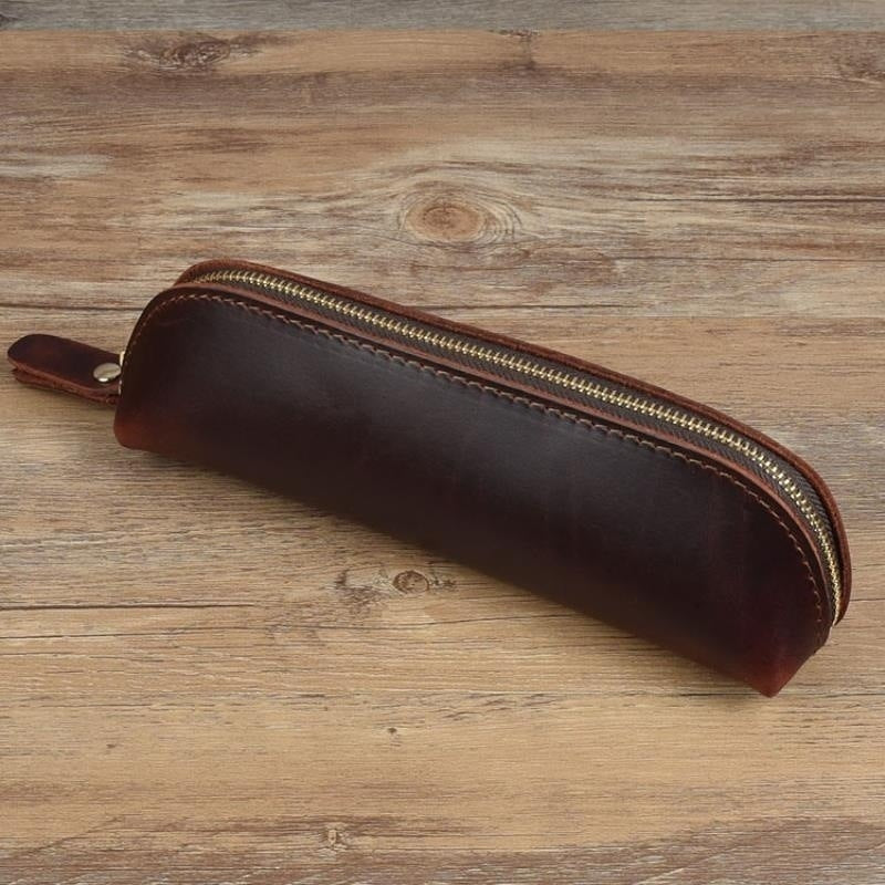 Brown leather pencil case with gold zipper on a wooden surface