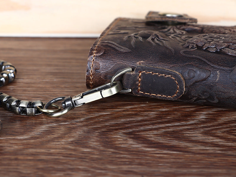 Brown leather wallet with floral embossing and metal chain on a wooden surface