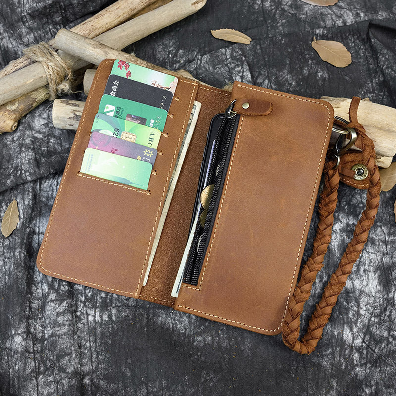 Brown leather wallet with card slots and a strap on a textured surface
