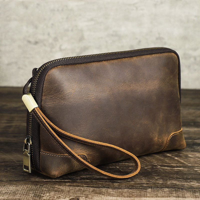 Brown leather clutch bag with a strap on a wooden surface