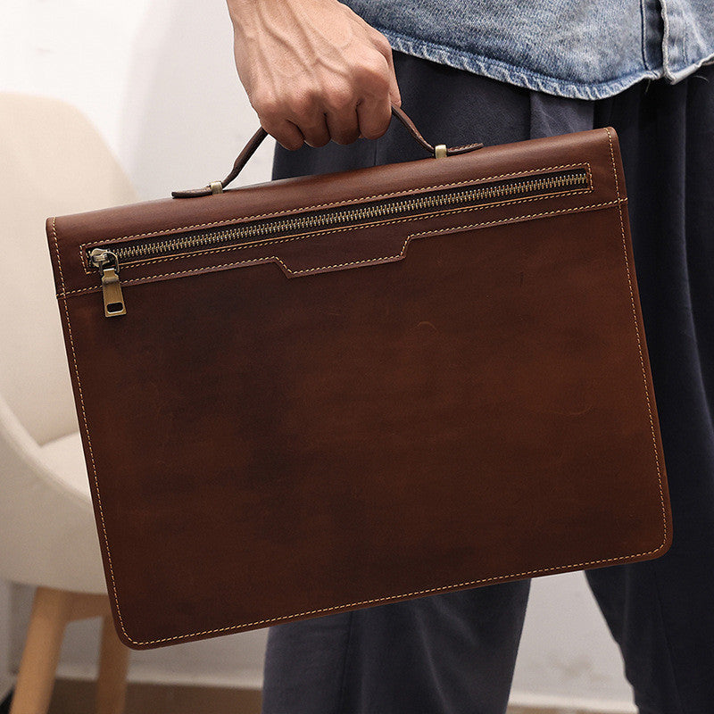 Brown leather briefcase held by a person wearing jeans and a denim jacket.