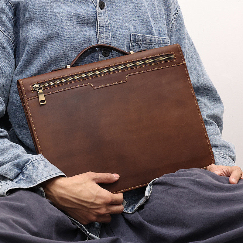 Person holding a brown leather briefcase with a light blue denim shirt.