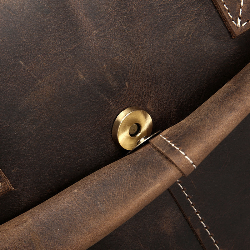 Close-up of a brown leather bag with a gold button and stitching detail.