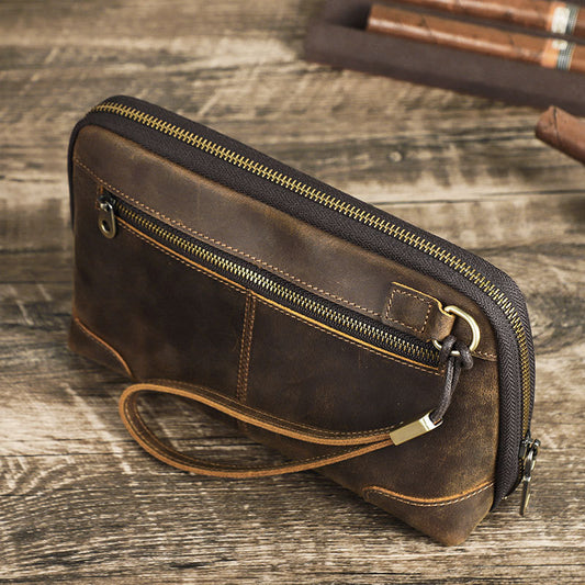 Brown leather clutch bag with gold zipper on a wooden surface