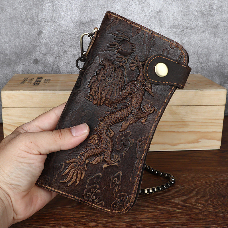 Brown leather wallet with dragon design held by a hand on a wooden surface.