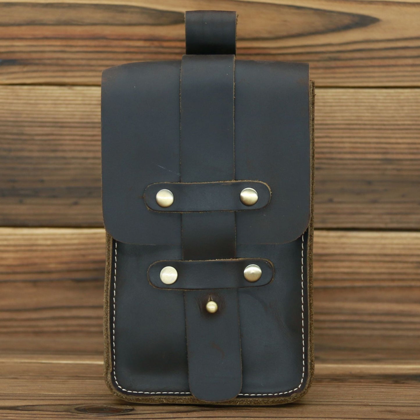 Dark gray leather pouch with gold buckles on a wooden background