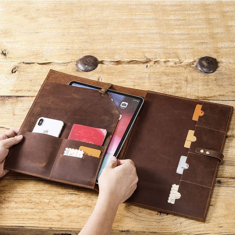 Brown leather wallet with compartments holding a phone, cards, and a tablet on a wooden surface.