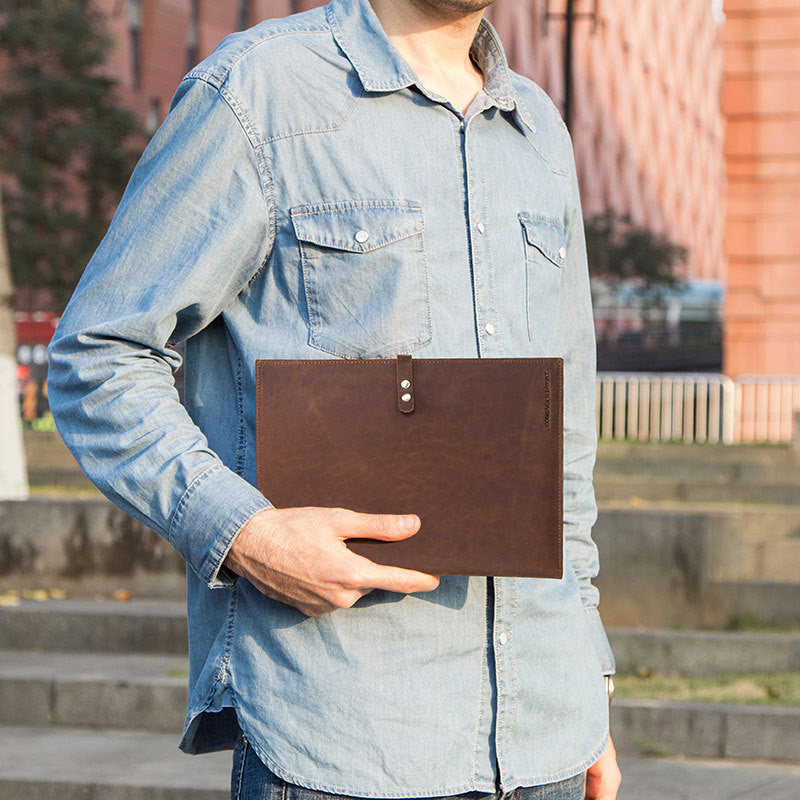 Person holding a brown leather folder outdoors with a blurred background