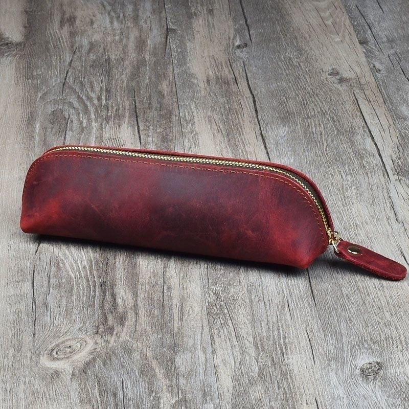 Red leather pencil case with gold zipper on a wooden surface
