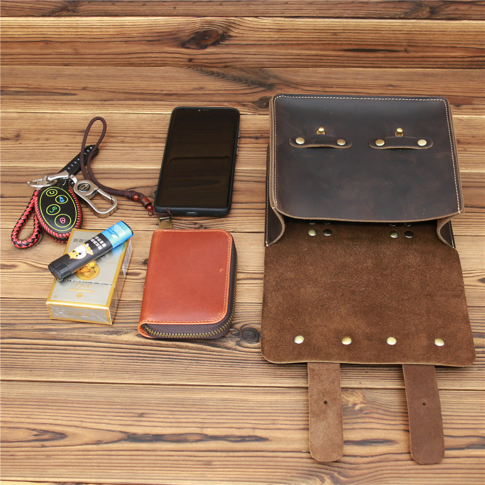 Brown leather bag with phone, wallet, and keychain on a wooden surface