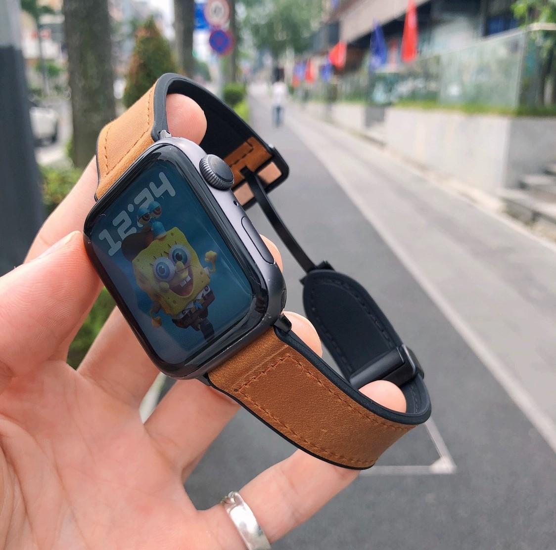 Smartwatch with a brown leather strap held by a hand on a city street.