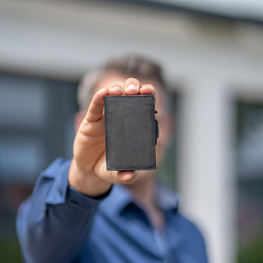 Person holding a black wallet in front of a blurred background
