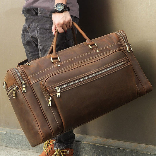 Person holding a large brown leather duffel bag against a neutral background