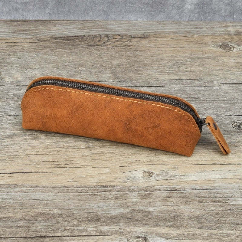 Brown leather pencil case with a zipper on a wooden surface