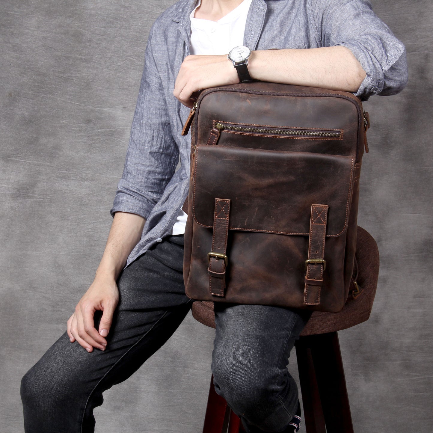 Person holding a brown leather backpack against a gray background
