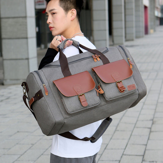Person carrying a gray duffel bag with brown leather accents on a city street.