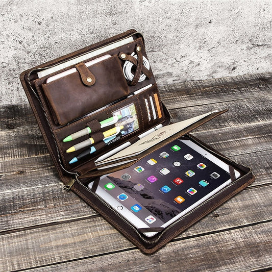 Brown leather organizer with tablet, pens, and other items on a wooden surface