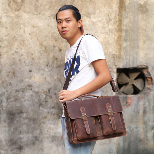 Man holding a brown leather satchel against a textured wall.