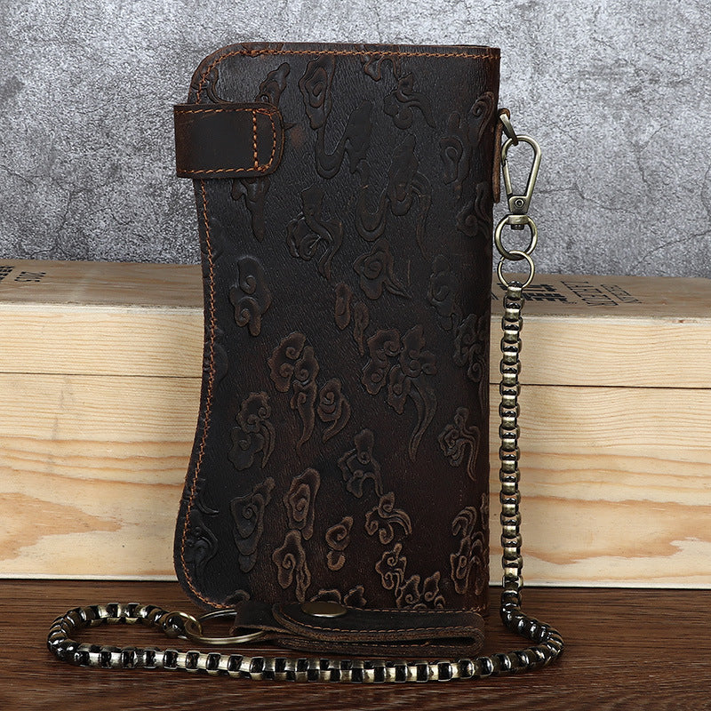 Brown leather wallet with floral pattern and chain strap on a wooden surface.