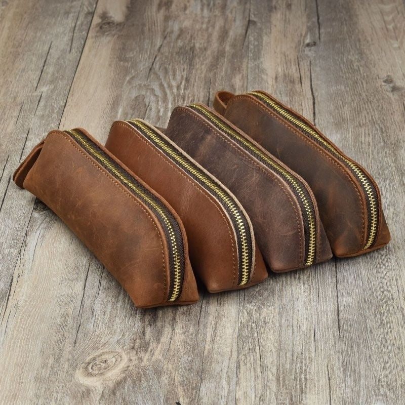 Set of four brown leather pouches with gold zippers on a wooden surface