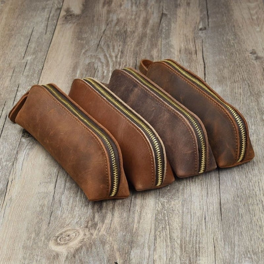 Set of four brown leather pouches with gold zippers on a wooden surface