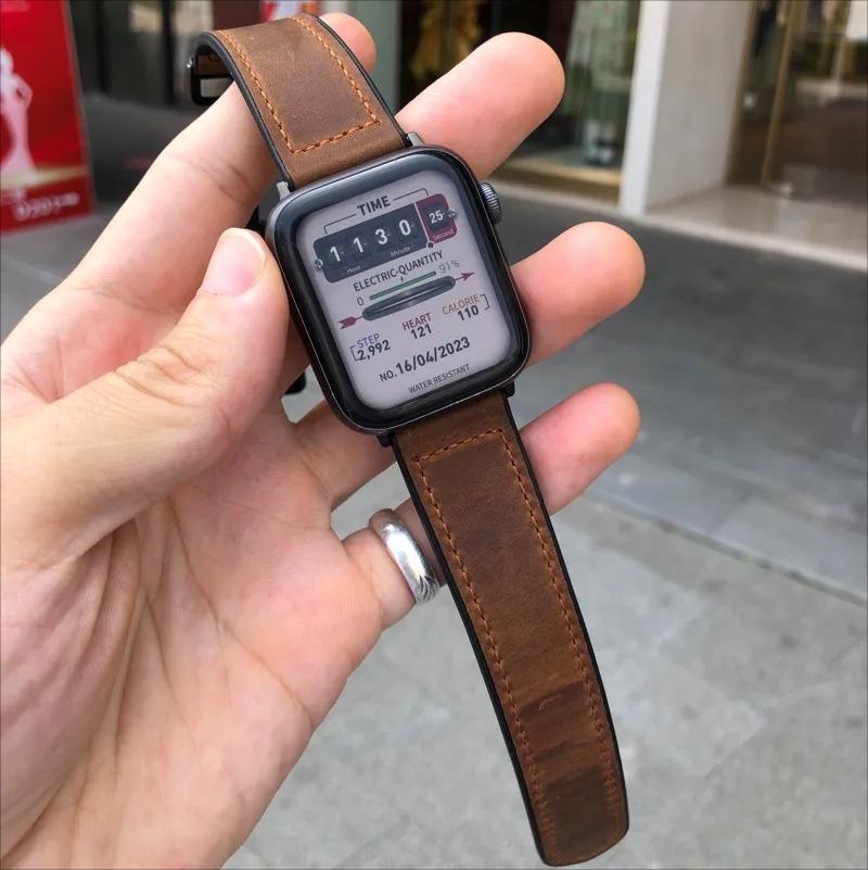 Smartwatch with a brown leather strap held in a hand outdoors.