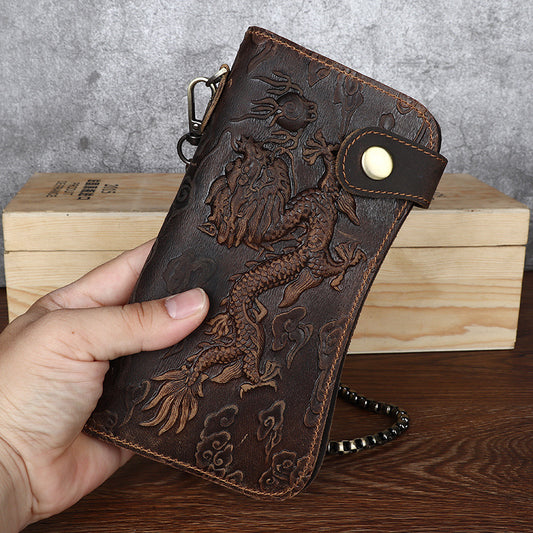 Brown leather wallet with dragon design held by a hand on a wooden surface.