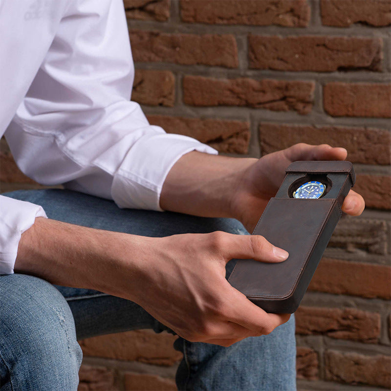 Person holding a leather-bound device with a compass against a brick wall.