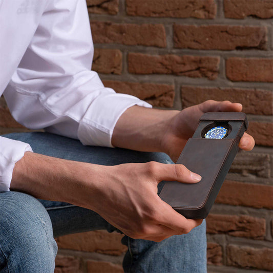 Person holding a leather-bound device with a compass against a brick wall.