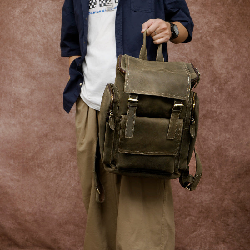Person holding a green leather backpack against a brown background